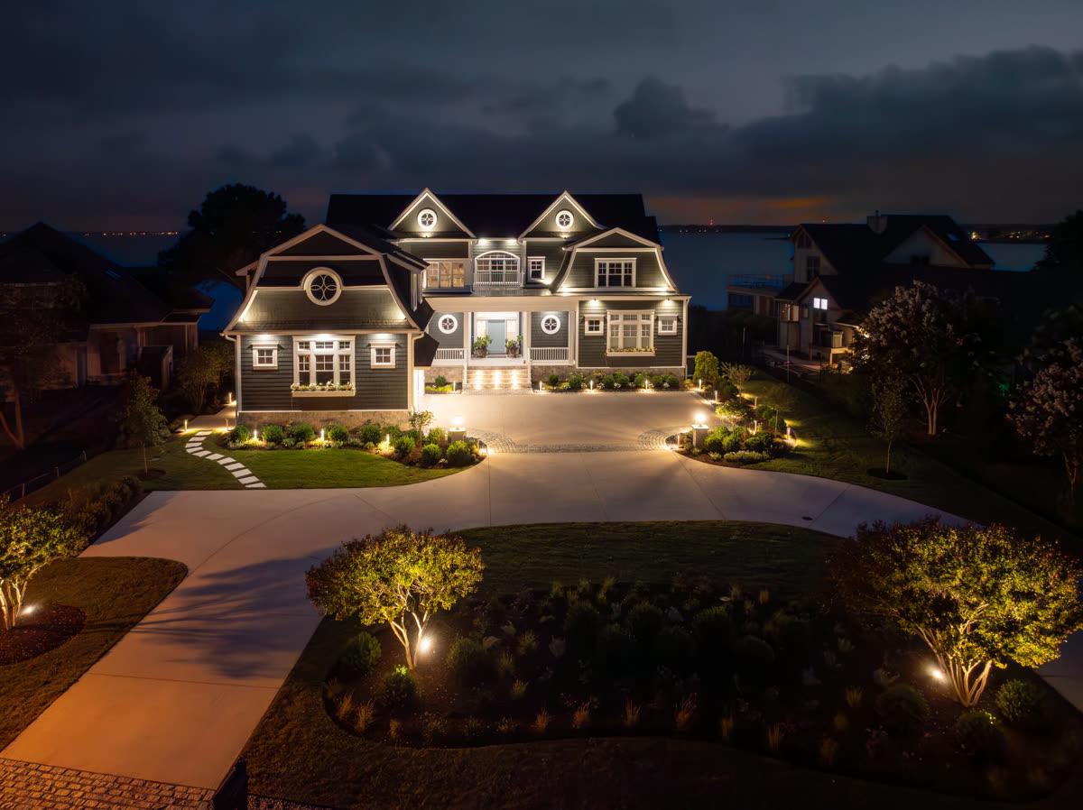 Coastal Source outdoor lighting illuminating a landscaped waterfront estate at night, showing the weather-engineered fixtures the brand is known for