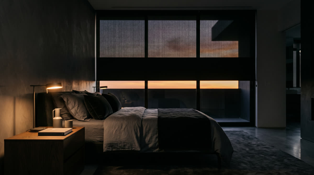 Motorized blackout shades half-descended in a luxury primary bedroom at sunset. Restrepo Innovations