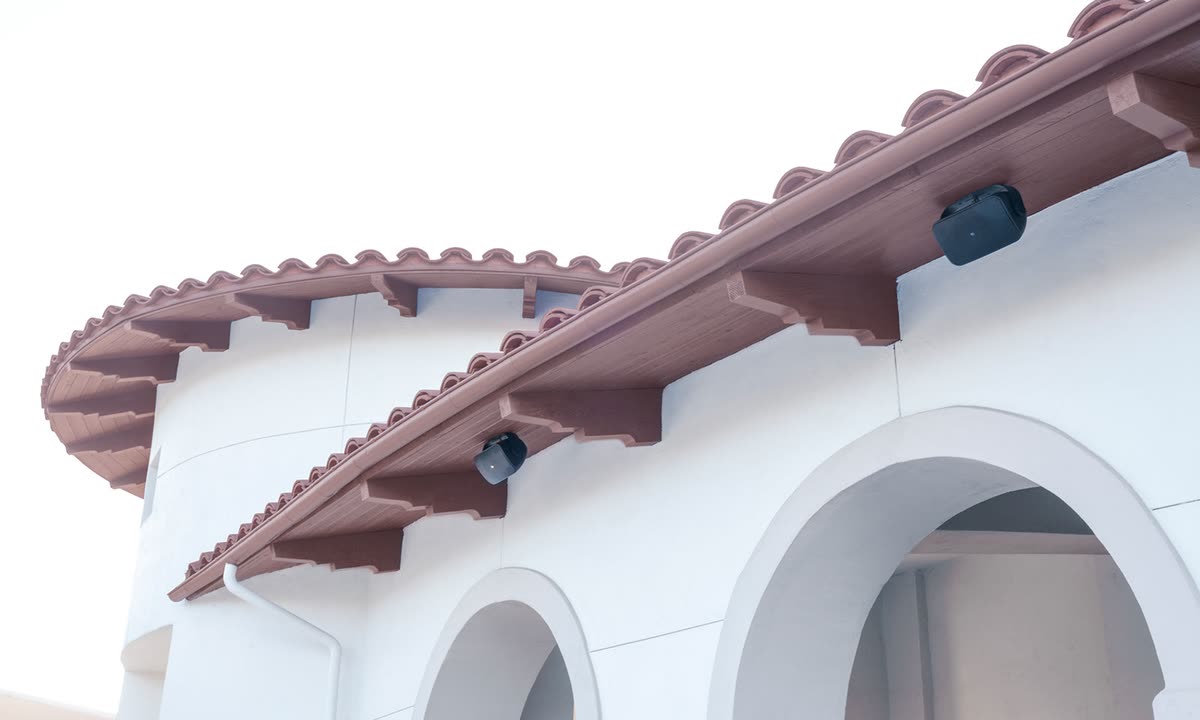 Surface-mount loudspeakers positioned beneath the covered eaves of a building